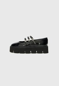 Black patent leather shoe with a thick black platform sole and three narrow straps across the vamp. Smooth texture, rounded toe design.