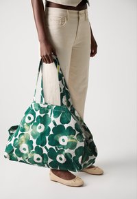 Große grüne Blumentasche aus Canvas, mit weitem Öffnungsbereich, langen Griffen und einem Muster aus dunkelgrünen und hellgrünen Blumen.