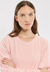 Sweatshirt rose à manches longues, côtelé, avec un décolleté en V et un tissu texturé. Les manches sont légèrement amples et l'ourlet est arrondi.