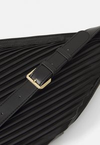 Borsa in pelle nera plissettata con superficie liscia. Presenta una tracolla nera regolabile e una fibbia dorata per la chiusura.