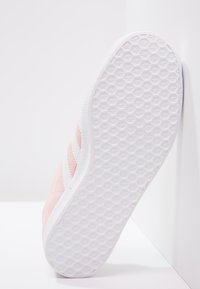 Růžové semišové tenisky s bílými pruhy, které mají texturovanou bílou gumovou podešev s hexagonálním vzorem pro lepší přilnavost a odolnost.