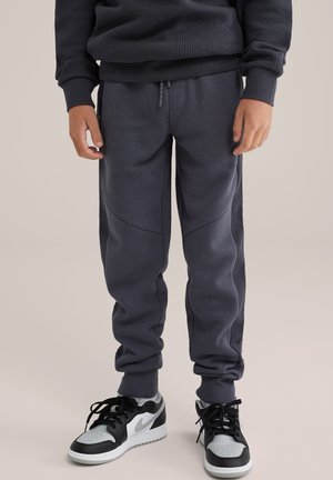 Donkergrijze joggers van een textiel met structuur, smal toelopende pasvorm, zijstrepen en elastische boorden, gecombineerd met zwart en grijze sneakers.