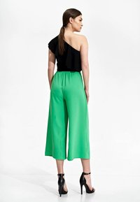 Czarna bluzka na jedno ramię z falbaną, zestawiona z zielonymi spodniami o szerokich nogawkach. Strój charakteryzuje się gładką teksturą i luźnym krojem. Czarne szpilki.