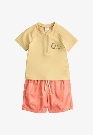 Conjunto de baño infantil de dos piezas con una camiseta de cremallera amarilla pálida que presenta un sol sonriente y el texto "Sigue al sol", combinada con pantalones cortos color coral estampados con soles.