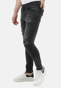 Zwarte gescheurde skinny jeans met rafelige zomen, gedragen met witte sneakers met een zwarte accent op de hiel.