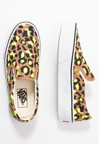 Scarpe Vans slip-on con una stampa leopardata marrone e nera, caratterizzate da macchie gialle vivaci, suola in gomma bianca e un accento nero lungo il bordo.