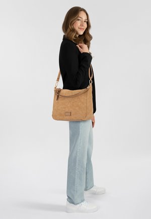 Braune Lederschultertasche mit strukturiertem Finish, angereichert mit einem verdrehten Tragegurt und einem Logo-Schild. Tragen zu hellblauen Jeans und weißen Sneakers.