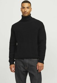 Schwarzer, gerippter Rollkragenpullover mit langen Ärmeln und tailliertem Schnitt, kombiniert mit dunkelblauen Jeans. Die Textur wirkt weich und warm.