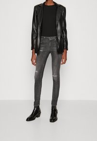 Blazer de cuero negro sobre una blusa negra, combinado con jeans ajustados grises con detalles rasgados. La modelo lleva botines negros.