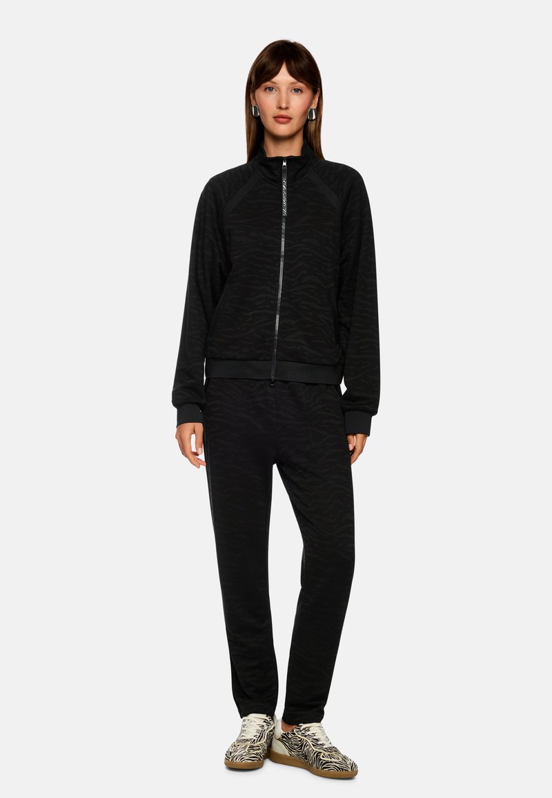 Black tracksuit with a subtle zebra pattern, zippered jacket, and matching tapered pants. Features ribbed cuffs and hem accents.