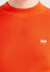 Pull orange côtelé avec un col rond et un petit logo blanc Levi's sur le côté gauche. Texture douce avec des rayures verticales.