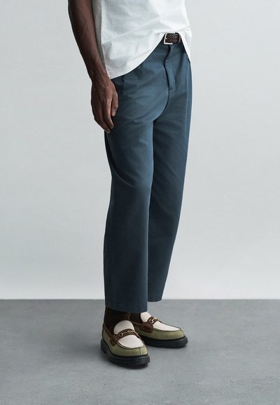 Pantaloni aderenti di colore blu scuro realizzati in un tessuto leggero, indossati con scarpe multicolori con un'accenno prominente e calze testurizzate.