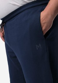 Navyfarbene Baumwoll-Jogginghosen mit elastischem Bund, Kordelzug, Seitentaschen und einem kleinen eingearbeiteten Logo am linken Bein. Glatte Textur.