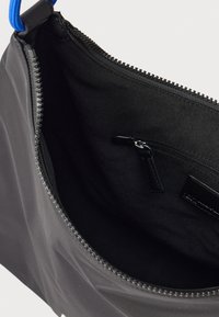 Μαύρη τσάντα με κλείσιμο με φερμουάρ και μπλε λαβή. Λείο εξωτερικό υλικό, μαύρο εσωτερικό με μικρή τσέπη με φερμουάρ και υφασμάτινη επένδυση.