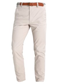 Pantalon slim beige clair avec poches avant, fermeture éclair et ceinture en cuir marron avec boucle métallique.