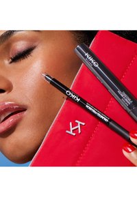 Svart eyeliner og grå blyant ligger ved siden av en rød kosmetikkpung med sølvskrift, mot en nærbilde av glatt hud og glansfulle lepper.