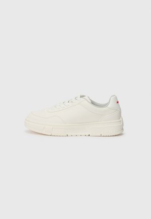 White sneakers with a smooth leather upper, round toe, flat laces, and a textured rubber sole. A red accent is on the heel.