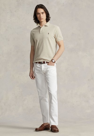 Béžové polo tričko s krátkym rukávom, biele džínsy, hnedé mokasíny, strieborné hodinky. Jednoduchý dizajn s logom na ľavej strane hrudníka. Hladká textúra.