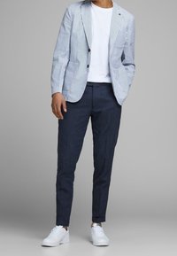 Striped blazer in light blue and white, paired with navy chinos and white sneakers. Blazer features two buttons and patch pockets.
