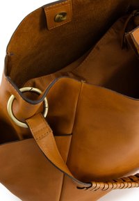 Braune Lederhandtasche mit strukturiertem Innenraum, goldenen Beschlägen und einem geflochtenen Tragegurt, mit einem Druckverschluss an der Oberseite.