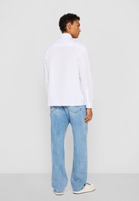 Hvid skjorte med en afslappet pasform, lange ærmer og side-slids, parret med lyseblå brede jeans og hvide sneakers.