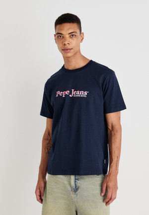 Camiseta de algodón azul marino con cuello redondo, mangas cortas y un logo frontal en texto rosa. Combinada con pantalones de denim en un tono azul claro.