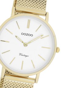 Montre avec bracelet en maille dorée, cadran blanc, index des heures dorés minimalistes, et le nom de la marque "OOZOO" au-dessus de "Vintage" en script.
