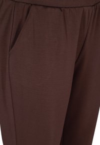 Braune, weiche Stoffhosen mit elastischem Bund und seitlicher Tasche; glatte Textur mit einem entspannten Schnitt.