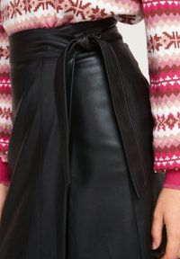 Falda de cuero negro con cinturón atado en la cintura, que presenta una textura suave y líneas limpias, combinada con un suéter rosa con estampado.