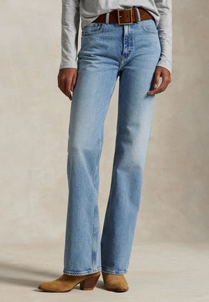 Un mannequin porte un jean bleu clair à jambes droites, une ceinture marron, un haut gris et des bottes à talons couleur beige.