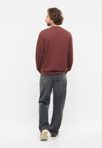 Bordeaux sweatshirt met een ronde hals, geribbelde mouwen en zoom, gecombineerd met grijze jeans en beige sneakers, bekeken vanuit de rug.