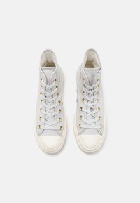 Zapatillas altas de lona gris claro con ojales dorados, puntera de goma blanca y cordones planos, que cuentan con una textura suave y un diseño sencillo.