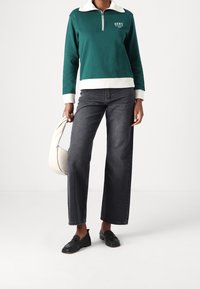 Sudadera verde con cremallera, cuello y puños blancos, combinada con unos pantalones vaqueros de pierna ancha oscuros y mocasines negros. Incluye un bolso blanco.