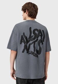T-shirt de algodão cinza com um corte solto, apresentando um grande texto abstrato preto nas costas que diz "ALLSAINTS LONDON." Mangas curtas, decote redondo.