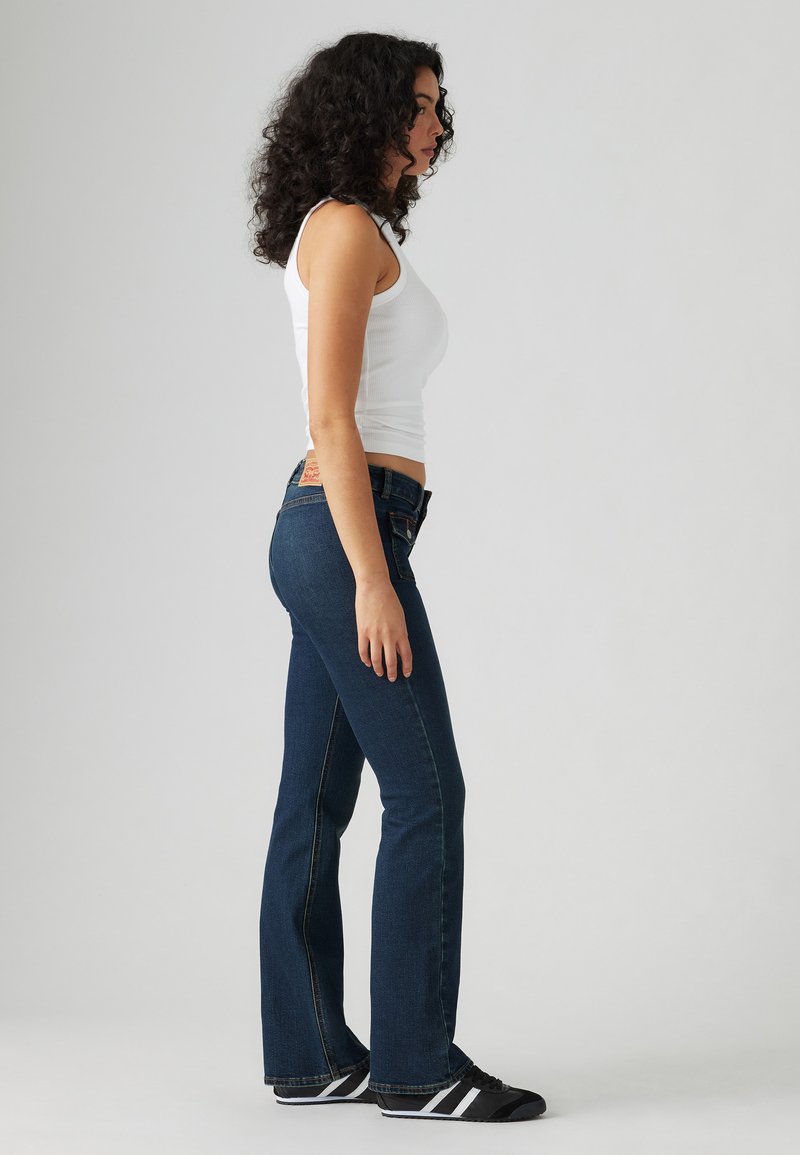 Schwarze, ausgestellte Jeans aus dunkelblauem Denim. Sie besitzen ein klassisches Fünf-Taschen-Design, einen leichten Glanz, gestickte Akzente und ein Leder-Backpatch.