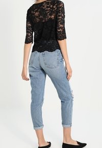 Top in pizzo nero con maniche a tre quarti, indossato sopra jeans azzurri chiari strappati, con orli arrotolati e scarpe nere flat.