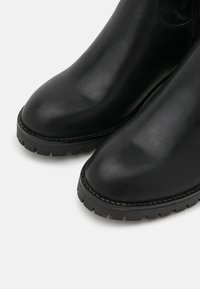 Botas de tobillo de cuero negro con un acabado suave, puntera redondeada y suela de goma resistente. Presentan costuras visibles a lo largo del borde.
