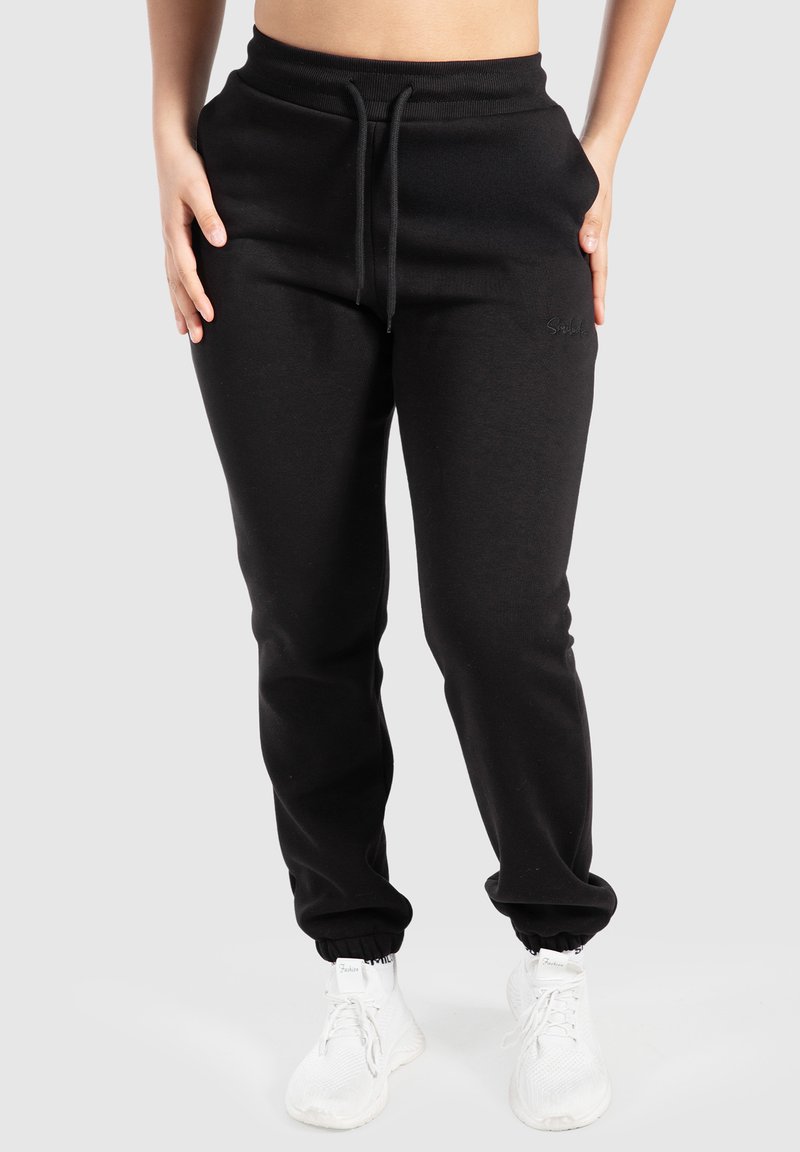 Zwarte joggingbroek gemaakt van zachte stof, met een elastische tailleband met trekkoord, boorden bij de enkels en een logo-detail aan de zijkant.
