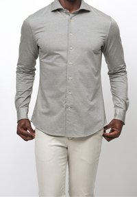 Ljusgrå långärmad skjorta med ett subtilt strukturerat mönster, knappstängning framtill och rundad nederkant. Kombinerad med beige byxor.