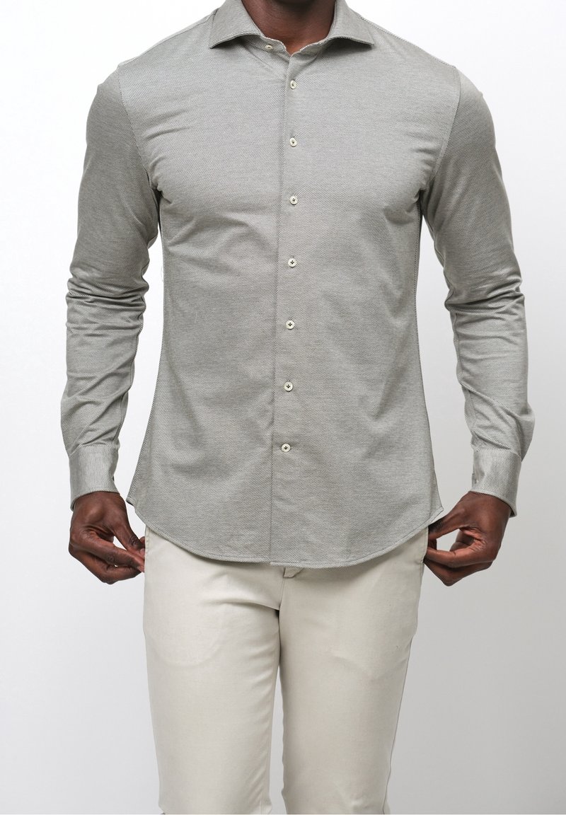 Ljusgrå långärmad skjorta med ett subtilt strukturerat mönster, knappstängning framtill och rundad nederkant. Kombinerad med beige byxor.