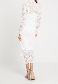 Weißes Spitzenkleid mit langen Ärmeln, hohem Kragen und einer Länge bis zur Mitte der Wade. Es verfügt über ein Blumenmuster und einen dezenten, durchsichtigen Überzug.