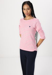 Stripete langermet skjorte i rosa og hvit med et marineblått hjerte-logo på brystet, sammen med marineblå bukser; glatt stoff, avslappet passform.