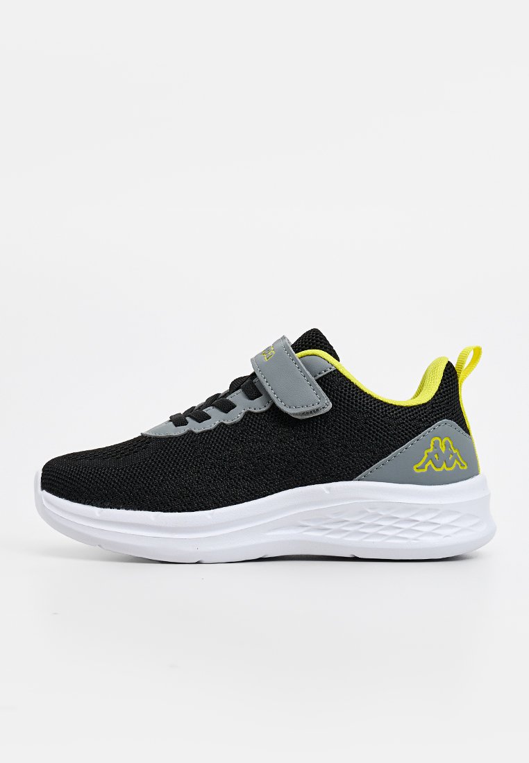 Schwarze und graue Kinder-Sneaker mit gelben Akzenten, weißer strukturierter Sohle, Klettverschluss und Logo an der Ferse vor einem weißen Hintergrund.