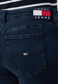 Mørkeblå denimjeans med en baklomme som har et brodert logo i rødt, hvitt og blått. Klassisk fem-lomdesignet, strukturert passform.