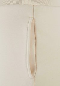 Leggings ajustados de color beige con una cintura acanalada, que cuentan con un bolsillo lateral de diseño oculto y textura suave. Material blando y elástico.