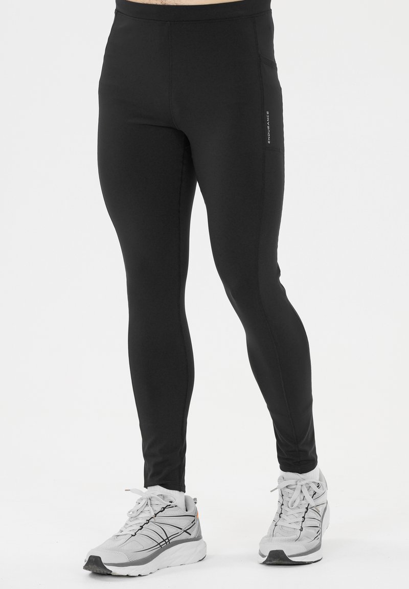 Svarta sportleggings med en tight passform, slät yta och reflekterande logotypdetalj. Åtföljt av grå löparskor.