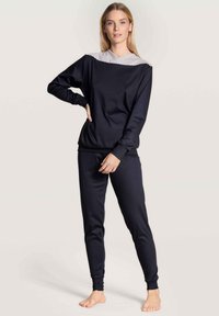 Svart lounge-set med långärmad topp med randig krage och matchande tajta byxor. Slät tyg, minimalistisk design.