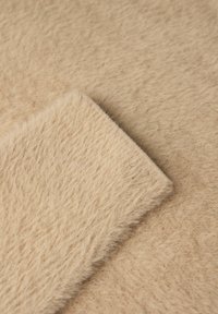 Beige konstpäls tyg med en mjuk, texturerad yta och fluffig plysch. Två överlappande bitar syns, vilket visar den enhetliga färgen och texturen.