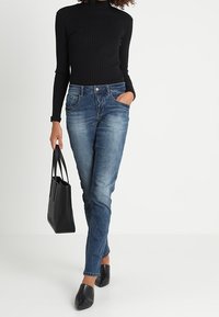 Czarna prążkowana bluzka z długim rękawem zestawiona z ciemnoniebieskimi, slim fit dżinsami. Czarna torebka i czarne buty wsuwane dopełniają strój.