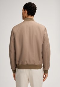 Giacca bomber color cammello con orlo e polsini a costine, caratterizzata da una texture liscia e un colletto a contrasto. Design semplice, senza decorazioni.